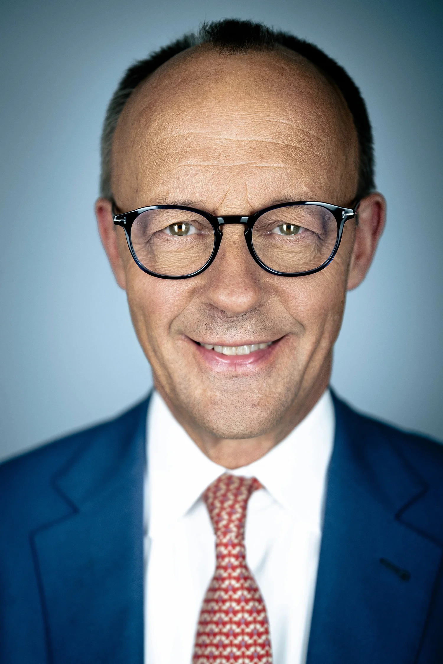 Politisches Portrait: Mann mit Brille und Anzug vor hellblauem Hintergrund